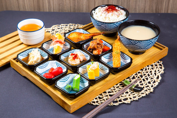 各式各样的日本食物:明台子鸡翅、面条汤、炸虾、酱汁、松脆蔬菜和猪肉片，用筷子盛在餐桌上餐巾侧面的木板上图片下载