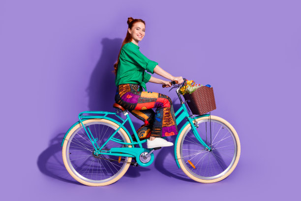 可爱可爱的女孩穿衬衫印花裤子骑自行车到空旷的空间孤立的紫罗兰色背景的全身照片图片下载