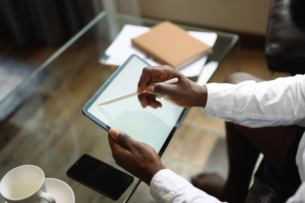 剪短照片的男性自由职业者坐在沙发上，在家里用数码平板电脑工作图片下载