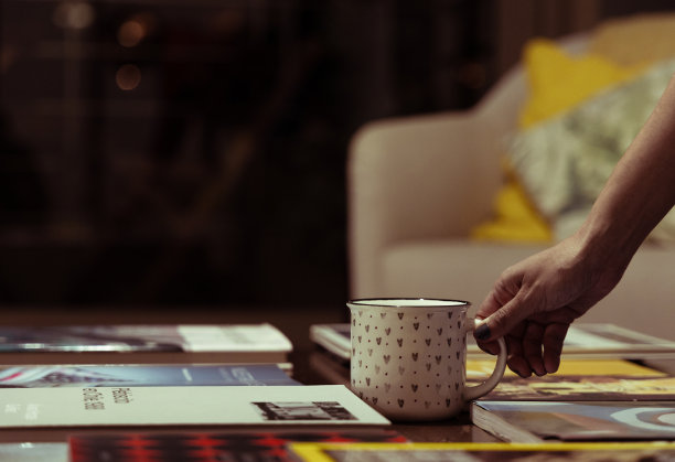 女人的手捧着杯子，桌子上堆满了书。秋天的下午。图片下载