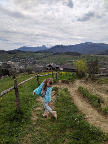 一个女孩站在一片盛开着春花的草地旁，背景是白雪覆盖的山脉。照片。图片下载