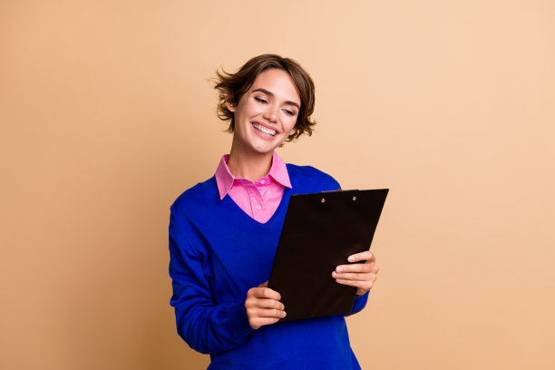 漂亮的年轻女孩的照片肖像拿着纸夹阅读文件简历穿着时髦的蓝色服装孤立的米色背景图片下载