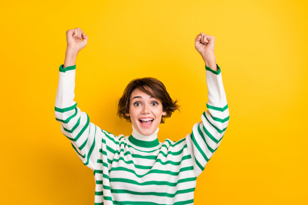 有趣的女士举手握拳庆祝大胜获得晋升的照片穿着条纹毛衣孤立的黄色背景图片下载
