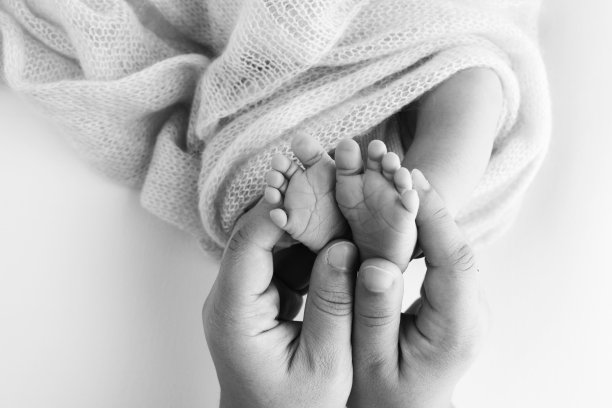 孩子的脚在妈妈手里，在爸爸手里，在父母手里。一个小新生儿的脚特写。小婴儿的腿。妈妈和她的孩子。幸福家庭概念。黑白图像的母性股票照片。图片下载