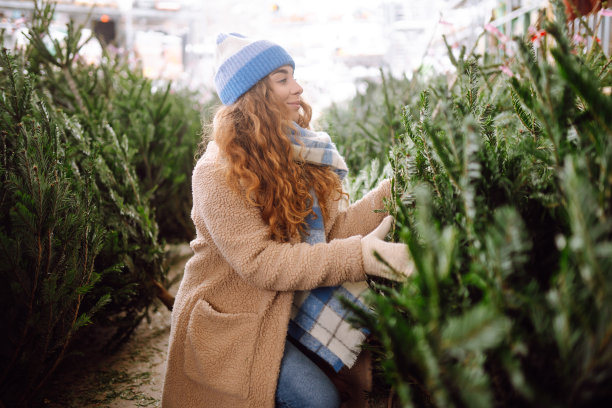一位微笑着的年轻女子正在挑选要买的圣诞树。图片下载