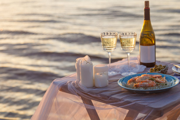 海滩上浪漫的日落晚餐。餐桌蜜月二人组与豪华的食物，一杯香槟饮料在餐厅与海景。夏日恋爱，浪漫约会就在度假概念上。图片下载