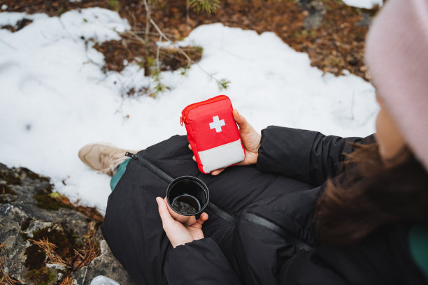 一个女人坐在森林里，手里拿着急救箱和一杯水，在丛林中生存的露营装备。图片下载