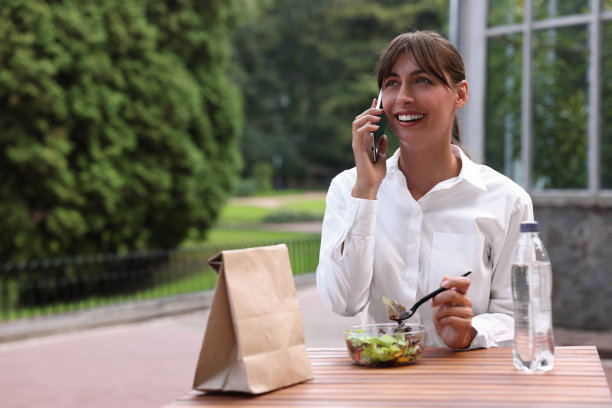 快乐的女商人一边用智能手机一边在户外的木桌边吃午餐，留出空间发短信图片下载