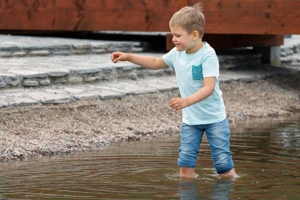 这是一幅可爱而欢快的小男孩在城市公园木桥附近玩水的照片图片下载