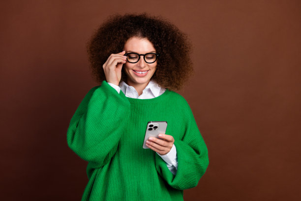照片迷人的积极的女士手触摸眼镜使用智能手机空的空间，并隔离在棕色背景图片下载