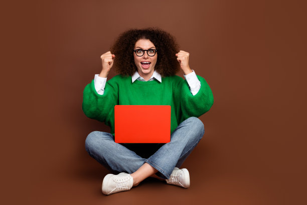 迷人的女士全身照片坐在地板上使用笔记本电脑举起拳头喊是的欢呼孤立在棕色的背景图片下载