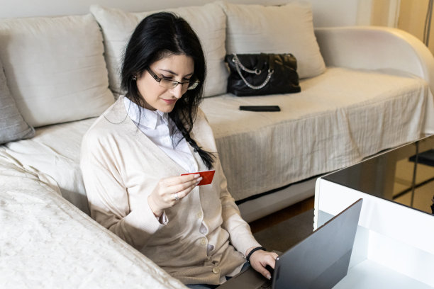 一个漂亮的年轻女子用信用卡网购的照片。她正在客厅的笔记本电脑上使用网上银行服务。图片下载