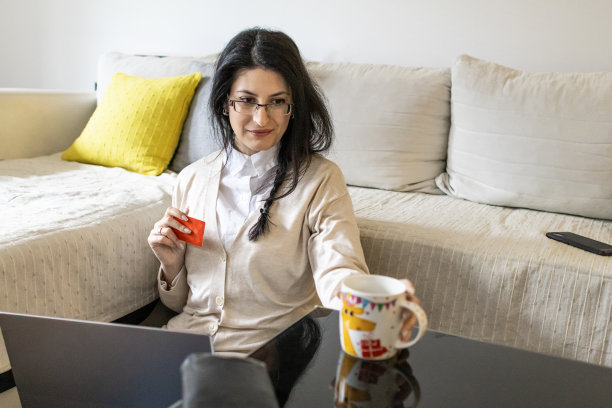 一个漂亮的年轻女子用信用卡网购的照片。她正在客厅的笔记本电脑上使用网上银行服务。图片下载