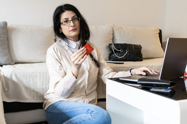 一个漂亮的年轻女子用信用卡网购的照片。她正在客厅的笔记本电脑上使用网上银行服务。图片下载