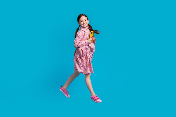 可爱小女孩的全身照片跳跃运动博主小女孩抱着智能手机上瘾的用户抖音孤立在蓝色背景图片下载