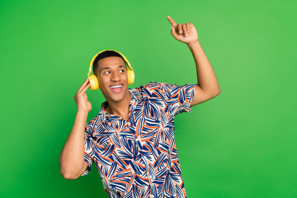 照片上乐观的男人穿着时髦的衣服，听着无线耳机，看起来空的空间，销售提供孤立的绿色背景图片下载