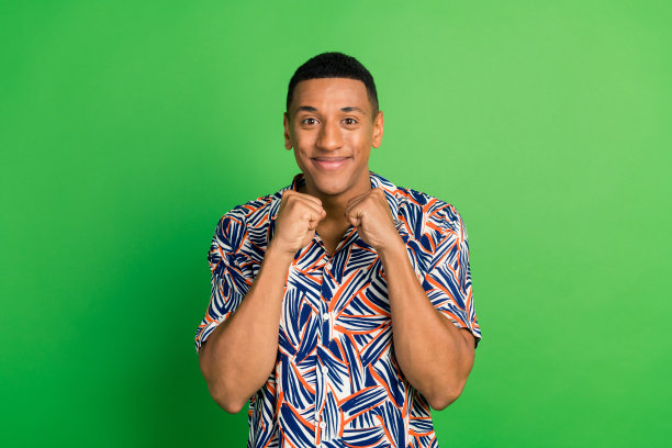 照片中，一个开朗的好男人穿着时髦的衣服，在绿色的背景下，露出双手、拳头和健身运动图片下载