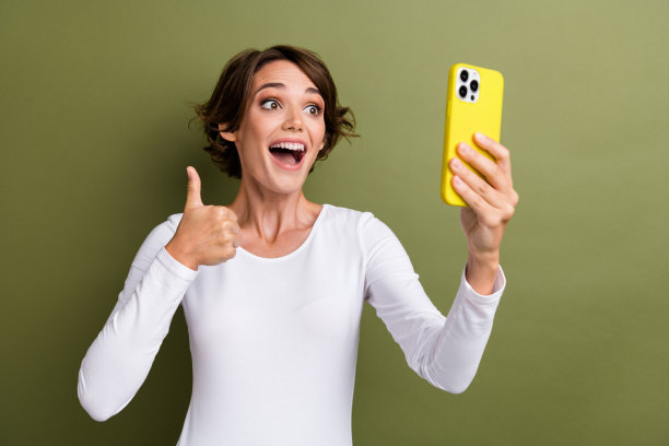 可爱的年轻女士的照片肖像拿着电话视频电话大拇指向上穿时髦的白色服装孤立的卡其色背景图片下载