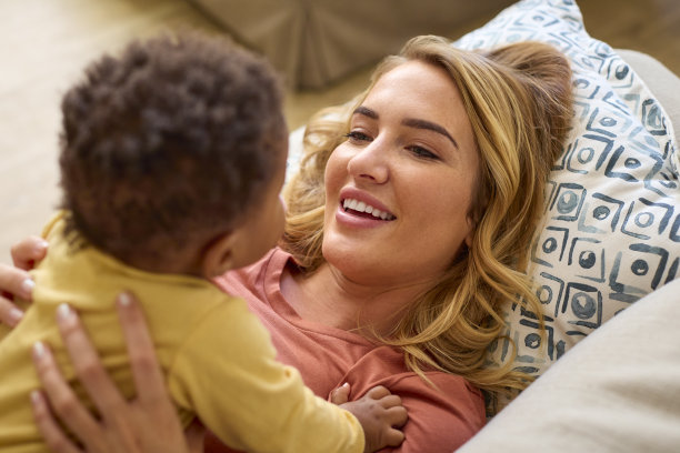 可爱的妈妈抱着一起躺在家里沙发上的女儿的俯拍照片图片下载