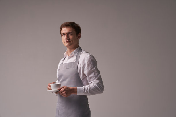 灰色背景上那个积极向上的男服务员。咖啡师为顾客端上一杯咖啡。一个成功年轻人的肖像。布局与复制空间。高质量照片图片下载