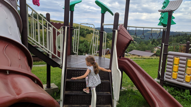 一个女孩在以山坡为背景的儿童滑梯上。照片。图片下载