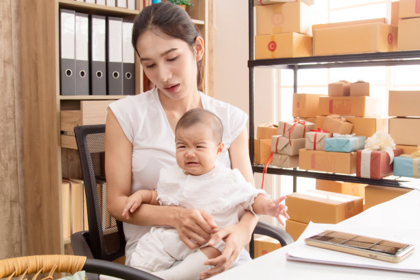 美丽的亚洲母亲在婴儿哭泣时抱着婴儿，妈妈不舒服地照顾孩子。年轻女性在家工作，单亲妈妈多任务自由工作的生活方式概念图片下载