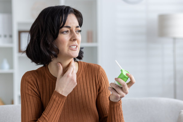 一个生病的年轻女子的特写照片，她感觉不舒服，坐在家里的沙发上，用手捂住喉咙，使用医用喷雾剂图片下载