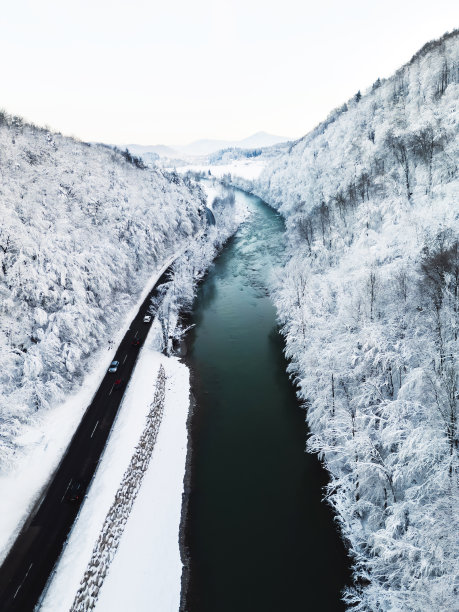 河流穿过山谷的垂直照片，两边都是白雪皑皑的冬季森林图片下载