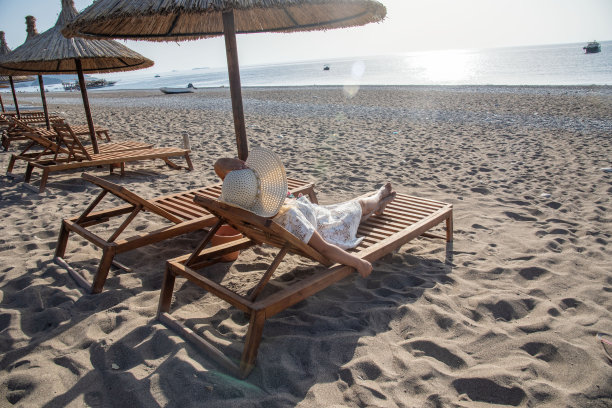 戴着白帽子躺在沙滩上的女人。戴着太阳草帽晒日光浴。夏季沙滩度假和度假旅游的概念。大海和蓝天的背景。图片下载