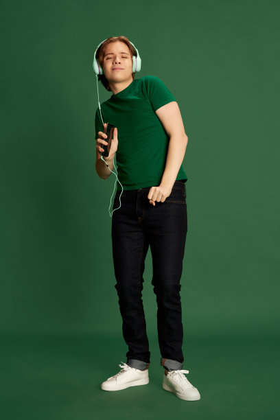 兴奋的年轻人戴着耳机，听着音乐，在绿色的背景下跳舞。最喜欢的旋律图片下载