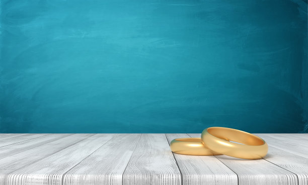 两个金戒指躺在靠近蓝色墙壁的木桌上的3d渲染，有很多复制空间。图片下载