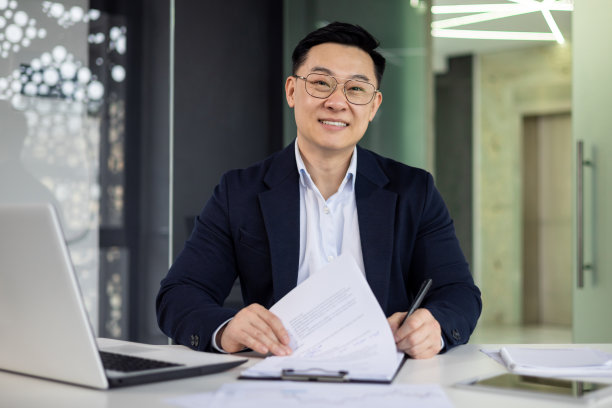 专业的亚洲商人在现代化的办公桌旁微笑图片下载