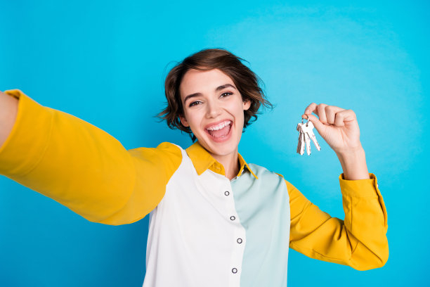 自拍照片年轻女子工作的房地产经纪人录制视频，大量的住宅小区公寓的钥匙被隔离在蓝色的背景图片下载