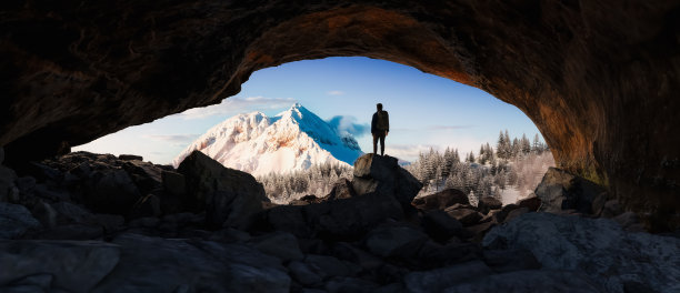 探险人站在岩石洞穴里。背景中的雪山景观。图片下载