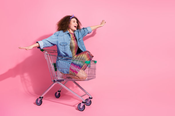 正面的全长照片无忧无虑的女士穿着牛仔装骑购物托盘手臂两侧空的空间孤立的粉红色背景图片下载