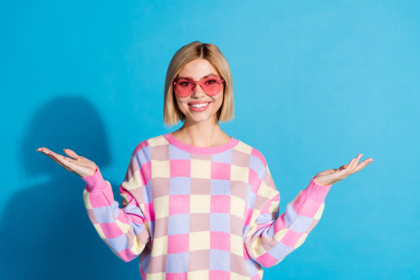 漂亮的年轻女孩的照片肖像太阳镜庆祝聚会双手空空间穿时髦的粉红色衣服孤立在蓝色的背景图片下载