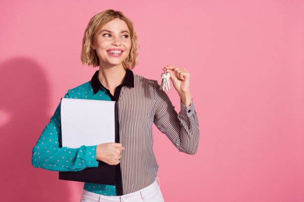 漂亮的年轻女孩的照片肖像拿着钥匙文件看起来空的空间穿着时髦的条纹青色的衣服孤立在粉红色的背景图片下载
