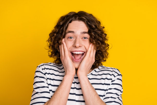 年轻时髦的高中生的特写照片，波浪头发的家伙触摸脸颊，情感反应孤立在黄色背景上图片下载