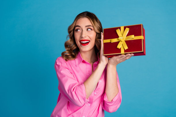漂亮的年轻女孩的照片肖像拿着兴奋的礼盒，看空的空间，穿时髦的粉红色衣服，发型孤立在蓝色的背景图片下载