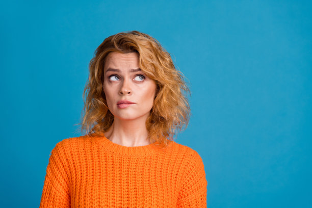 照片中，忧郁、体贴、可爱的女人穿着时髦的橙色衣服，在蓝色的背景上显得空荡荡图片下载