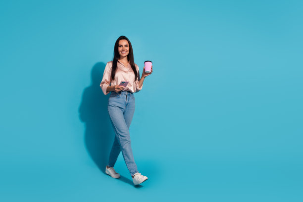 西班牙女子全身照片，穿着丝绸衬衫，拿着拿铁咖啡，走在蓝色背景上的空白空间图片下载