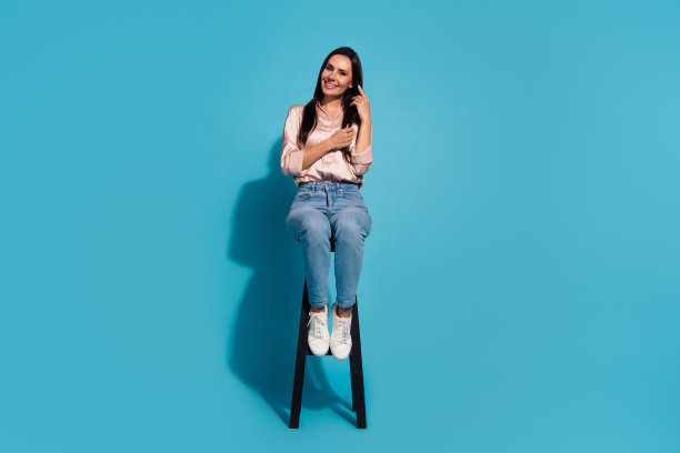 甜美可爱的女士全身照片穿着米色衬衫，坐在凳子上享受护发孤立的蓝色背景图片下载