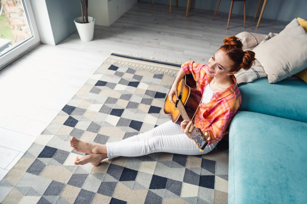 全尺寸高角度观看照片积极漂亮的女孩坐在地板上弹吉他看窗户灵感平里面图片下载