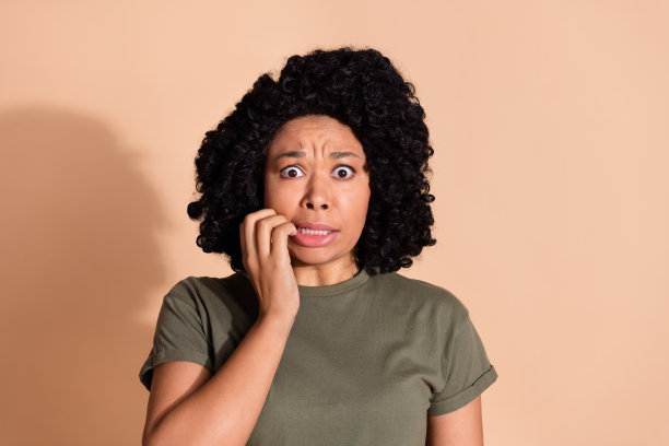 漂亮的年轻女子的照片肖像咬指甲害怕穿着时髦的卡其布衣服孤立的米色背景图片下载