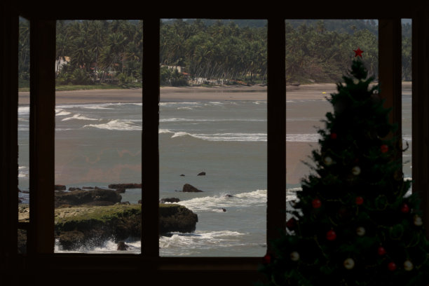 这是一幅蒙太奇照片，窗户旁边有一棵圣诞树的剪影，背景是阿拉戈斯海岸的景色，将南半球国家的圣诞节庆祝活动概念化，图片下载