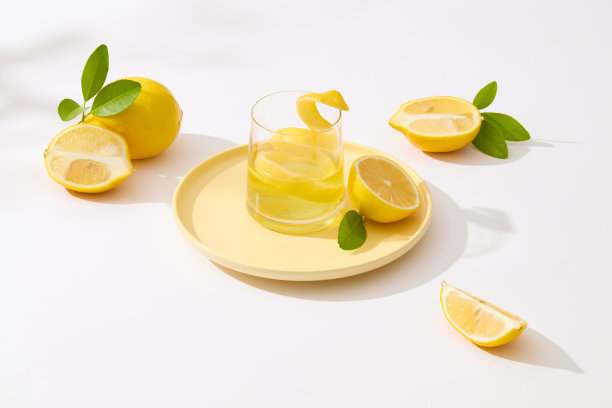 一个黄色的圆形盘子放在照片的中心，上面有一杯柠檬汁和一个柠檬片，用白色平面的柠檬片装饰。复制空间，高角度图片下载