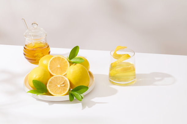 柠檬主题照片，一些柠檬在一个圆形的白色盘子上，装饰着一罐蜂蜜和一杯柠檬汁，里面有柠檬皮。前视图，拷贝空间图片下载