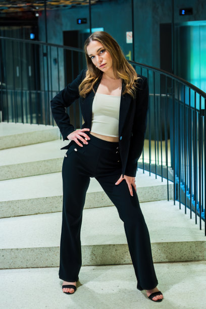 穿着经典裤子套装的美女站在螺旋楼梯上，双手放在臀部和大腿上图片下载