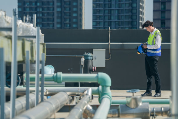 专业工程师在被管道和管道系统包围的建筑物屋顶上通过对讲机进行通信。图片下载