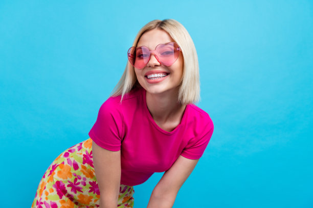 照片肖像迷人的年轻女子太阳镜摆模特穿着时尚的粉红色衣服孤立的蓝色背景图片下载